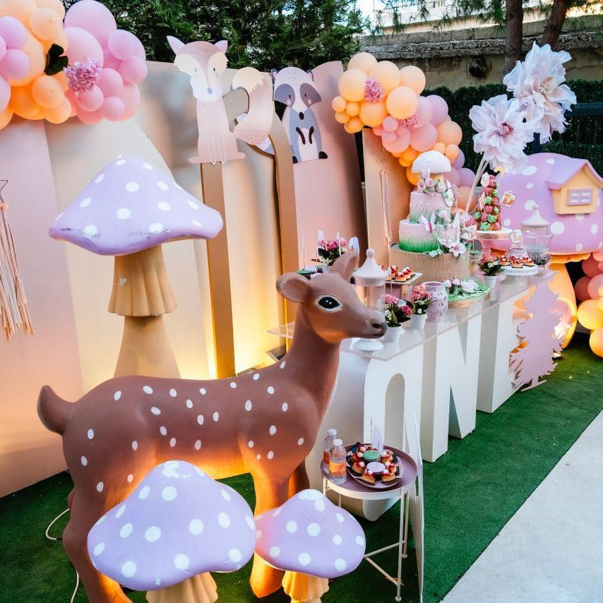 Decorative setup with balloons, a deer figure, and a cake on a table outdoors.