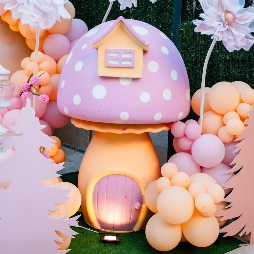 Decorative setup with a polka dot mushroom house, balloons, and flowers.