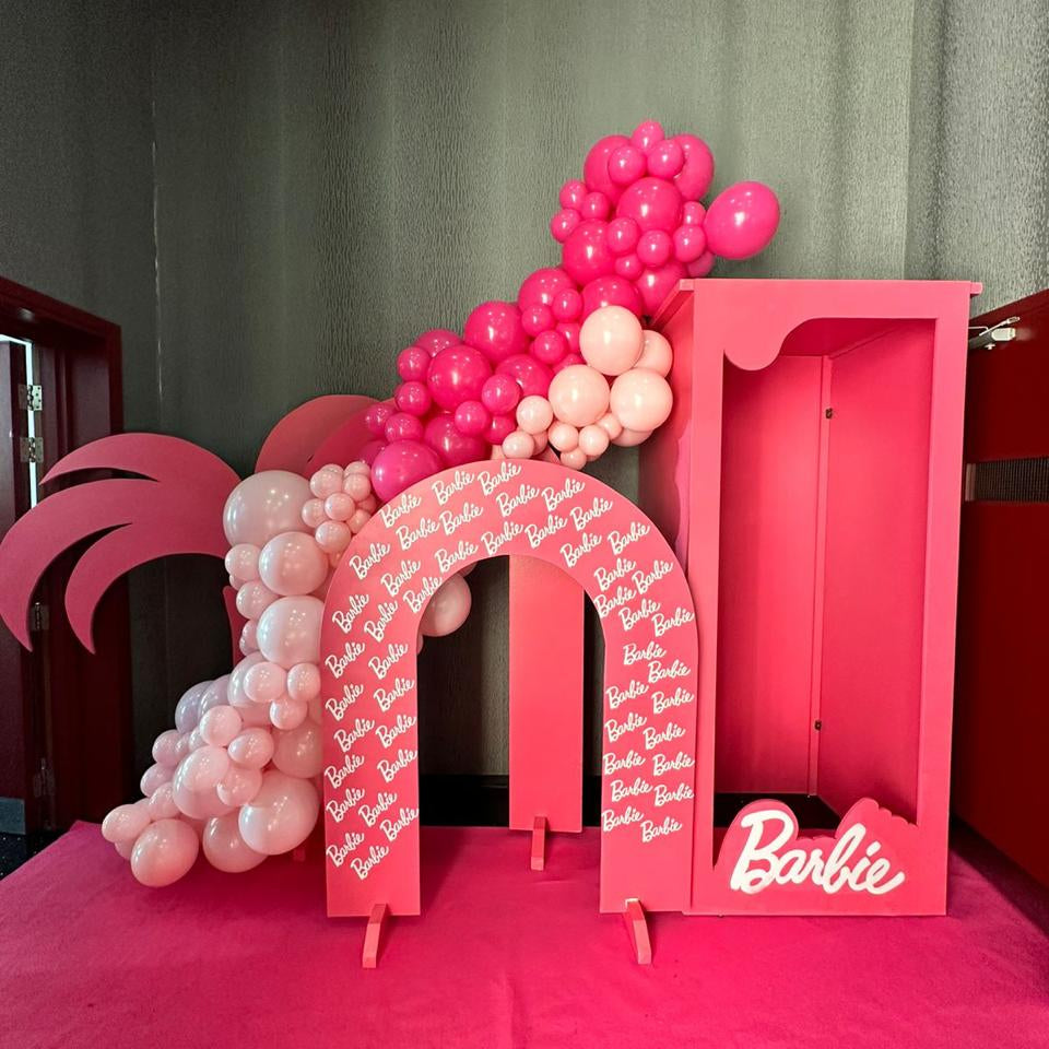 Pink arch with balloons and a Barbie box against a green curtain