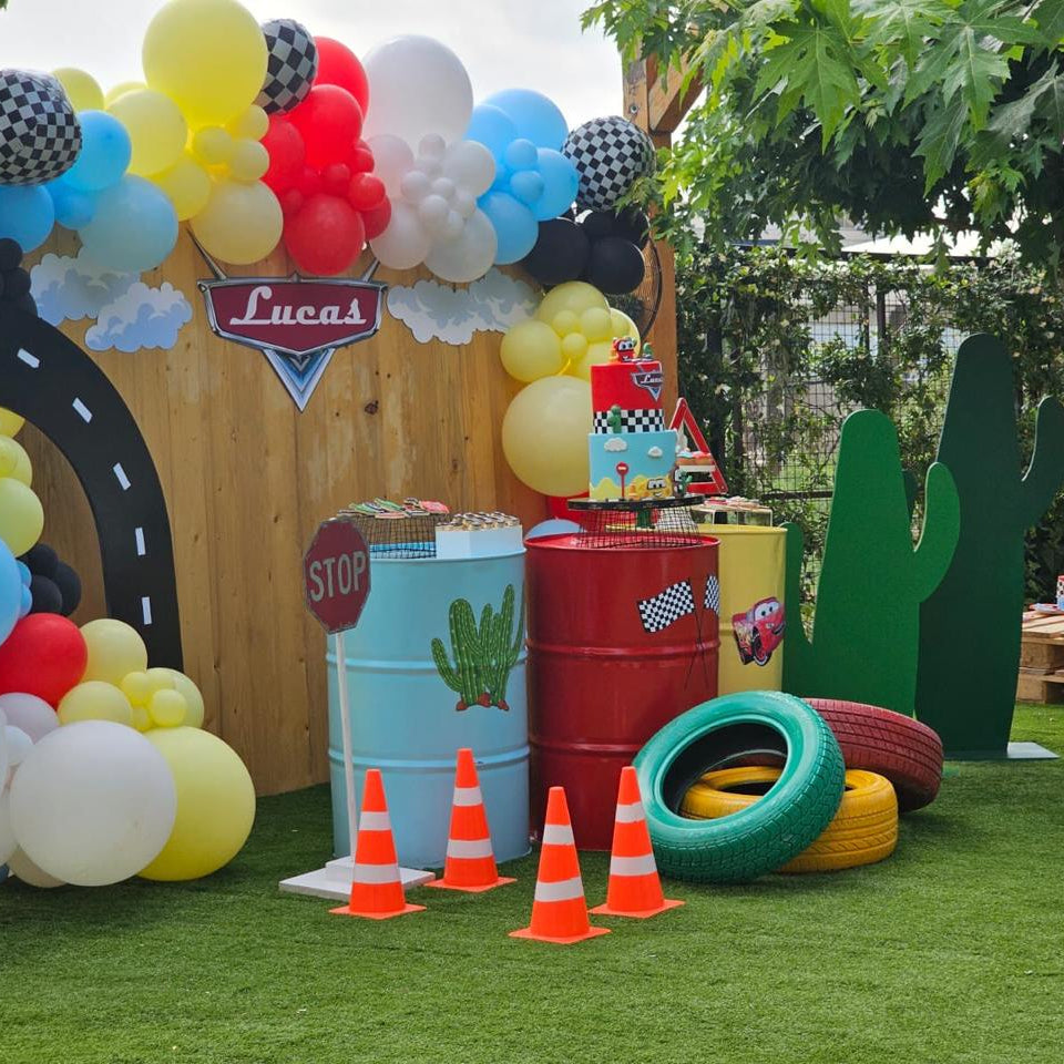 Colorful outdoor setup with balloons, barrels, and traffic cones on a grassy area.
