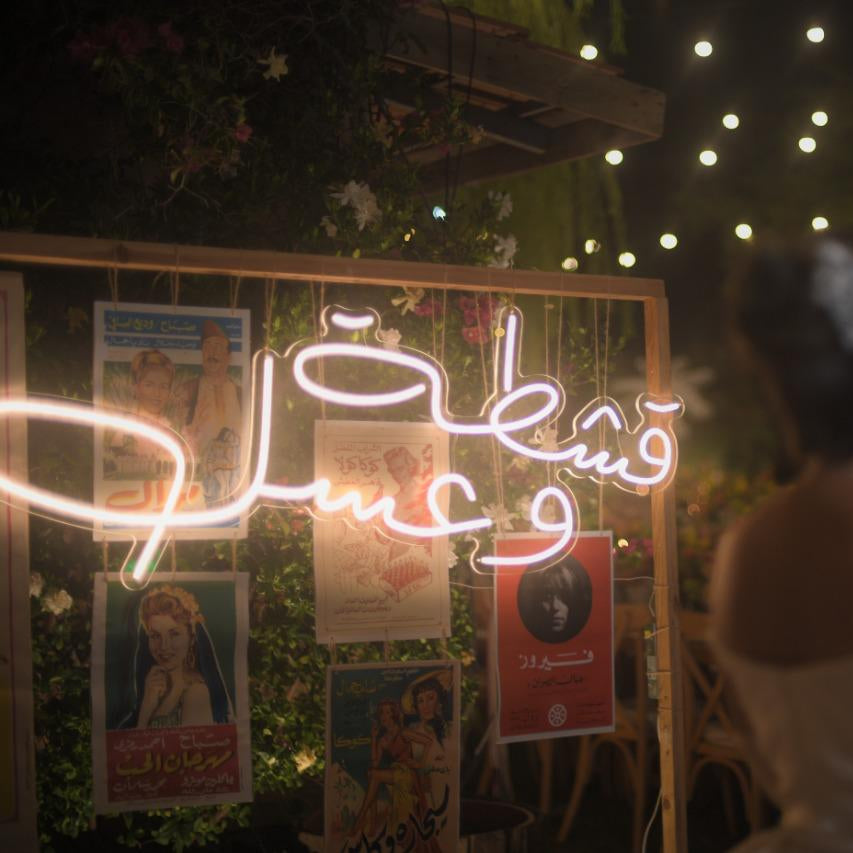 Neon sign with Arabic text in a romantic setting with a couple and fairy lights.