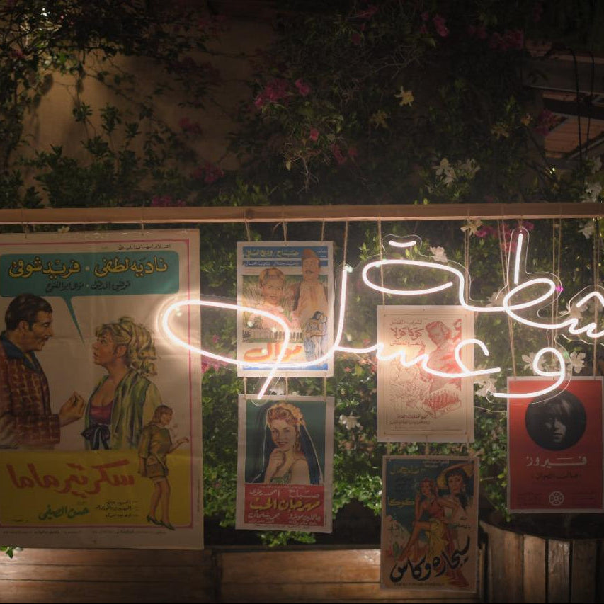 Neon sign with Arabic text and framed posters on a decorative wall.