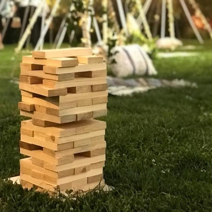 Wooden Jenga game set on grass with decorative lights and people in the background