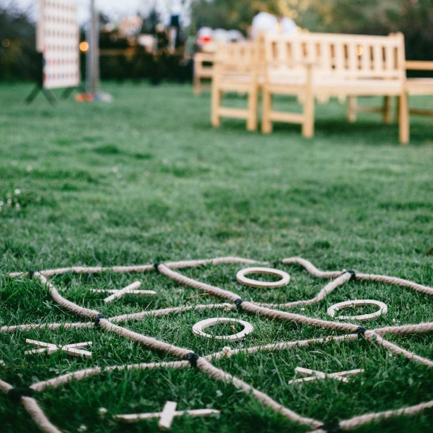 Outdoor setting with a rope maze on grass, blurred background of trees and people.