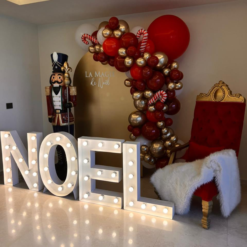 Decorative setup with 'NOEL' letters, balloon arch, and Christmas-themed chair.
