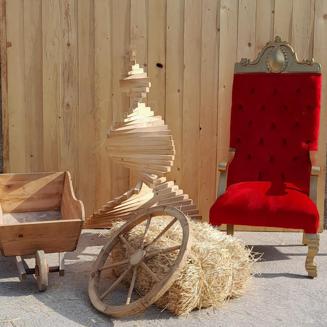 Wooden cart with hay, wooden box, and red velvet chair against a wooden wall.