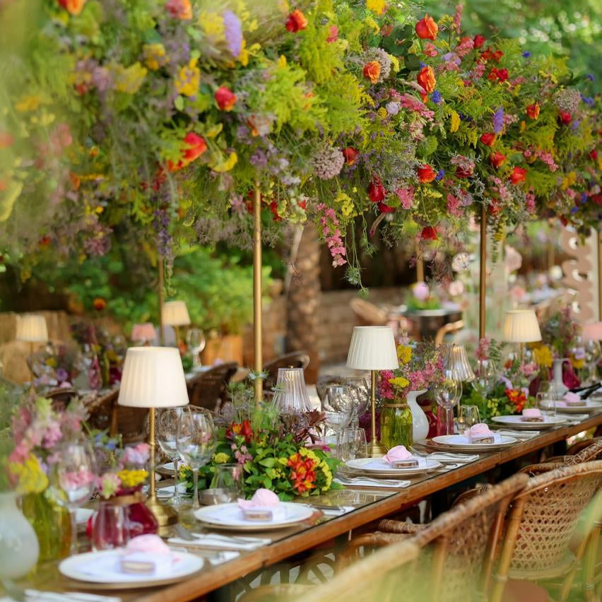 Decorative outdoor table setting with flowers and lamps in a garden.