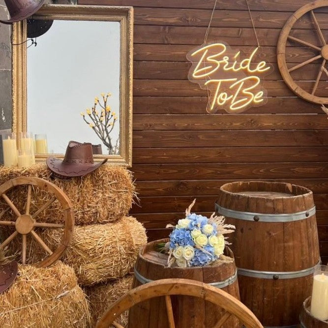Rustic wedding setup with hay bales, barrels, and 'Bride To Be' sign.