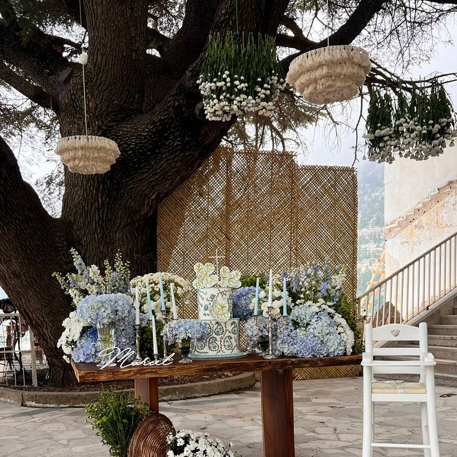 Decorative outdoor setting with flowers, table, and chairs under a large tree.