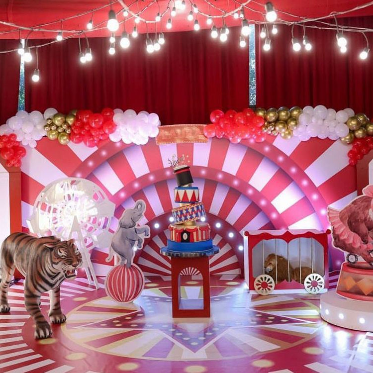 Carnival-themed decor with striped arch, balloons, and animal figures on a red and white floor.