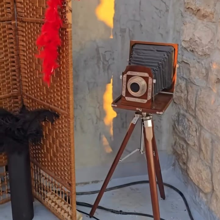 Vintage camera on a tripod with a stone wall and fire in the background